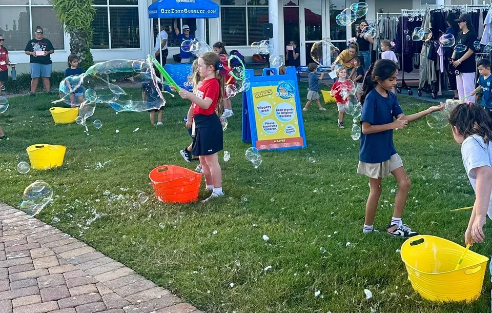 Kids wave bubble wands on a lawn during an outdoor community event