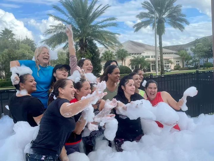 A group of adults laughing in a foam pit outdoors on a sunny day